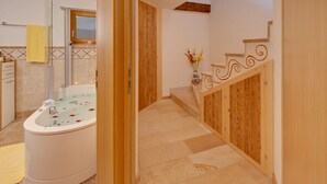 Une salle de bain avec une baignoire, un lambris en bois, un carrelage au sol et un escalier en bois.