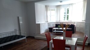 A modern living room with a dining table, red chairs, a sofa, and a window with curtains. - Villa Birkenfeld (Birkenfeld)