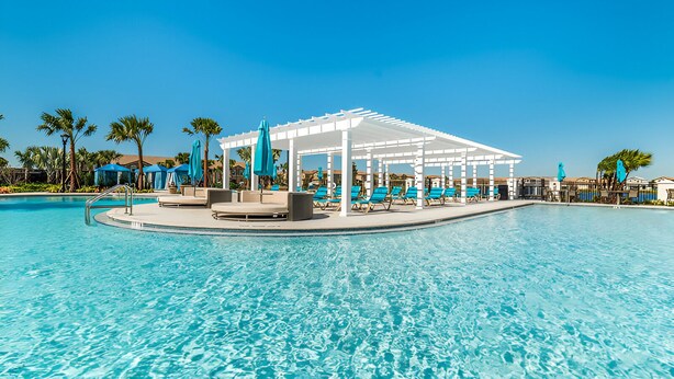 A pool area with a covered seating area, lounge chairs, and umbrellas.