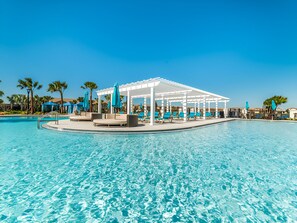 A pool area with a covered seating area, lounge chairs, and umbrellas.