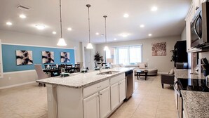 A modern kitchen with a large island, pendant lighting, and a dining area with a sofa and table.