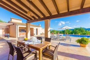 A covered outdoor patio with a dining table set for two, surrounded by wicker chairs.