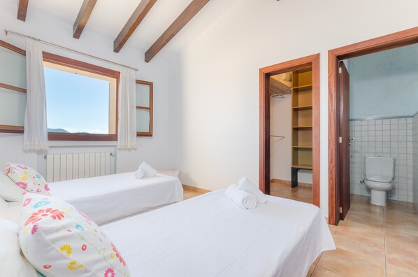 A bedroom with two beds, a window with curtains, a wooden ceiling, and a view of the outside.