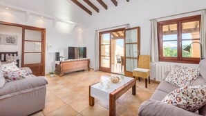 A spacious living room with a sofa, a coffee table, and a TV. There is a sliding glass door leading to an outdoor area. - NA MAIANS - Villa with private pool in Canyamel. Free WiFi (Canyamel)