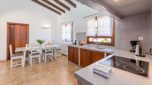 A modern kitchen with wooden cabinets, a built-in stove, and a dining area with a table and chairs. - NA MAIANS - Villa with private pool in Canyamel. Free WiFi (Canyamel)