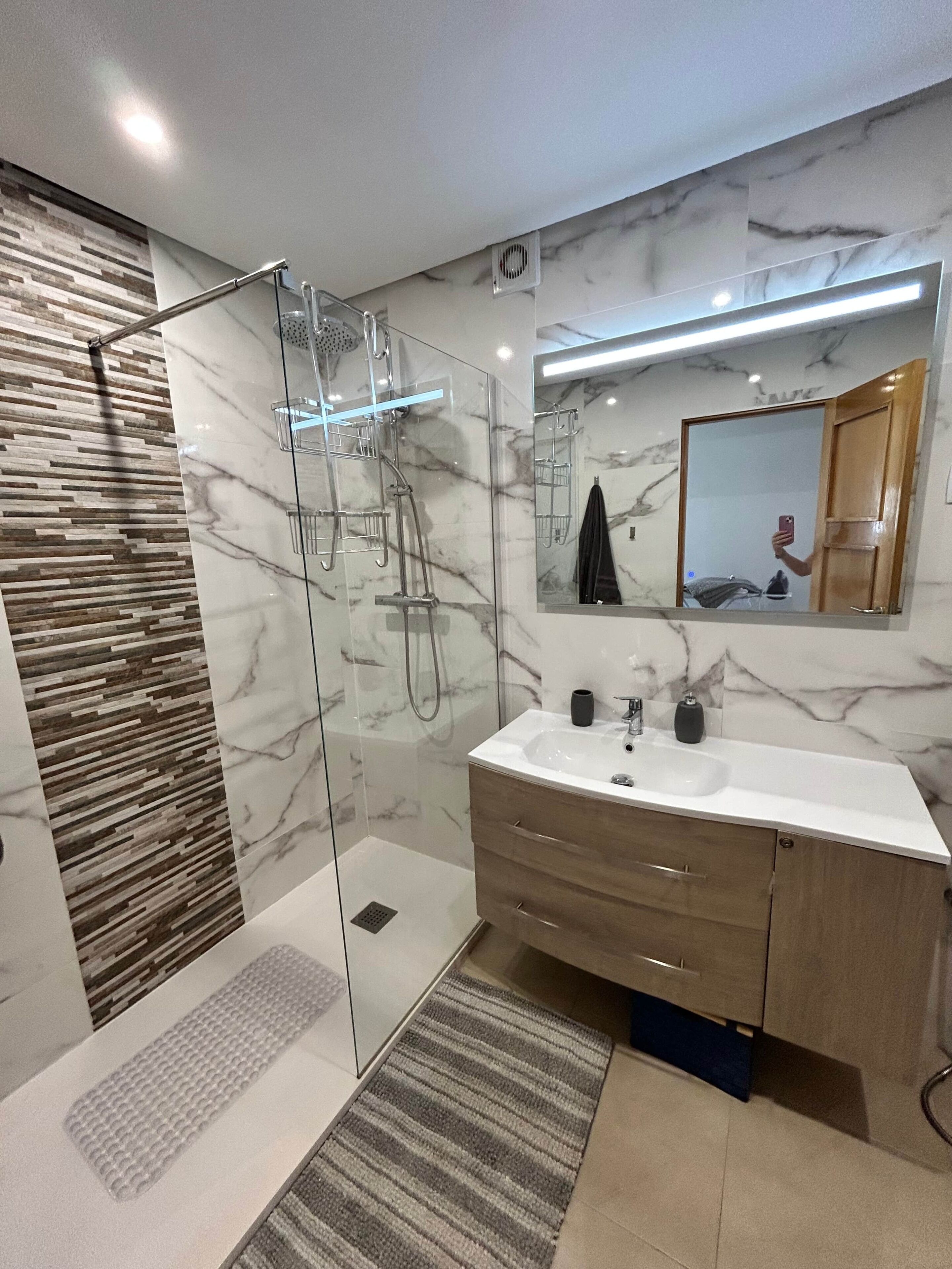 A modern bathroom with a glass-enclosed shower, a marble backsplash, a vanity with a sink, and a mirror.