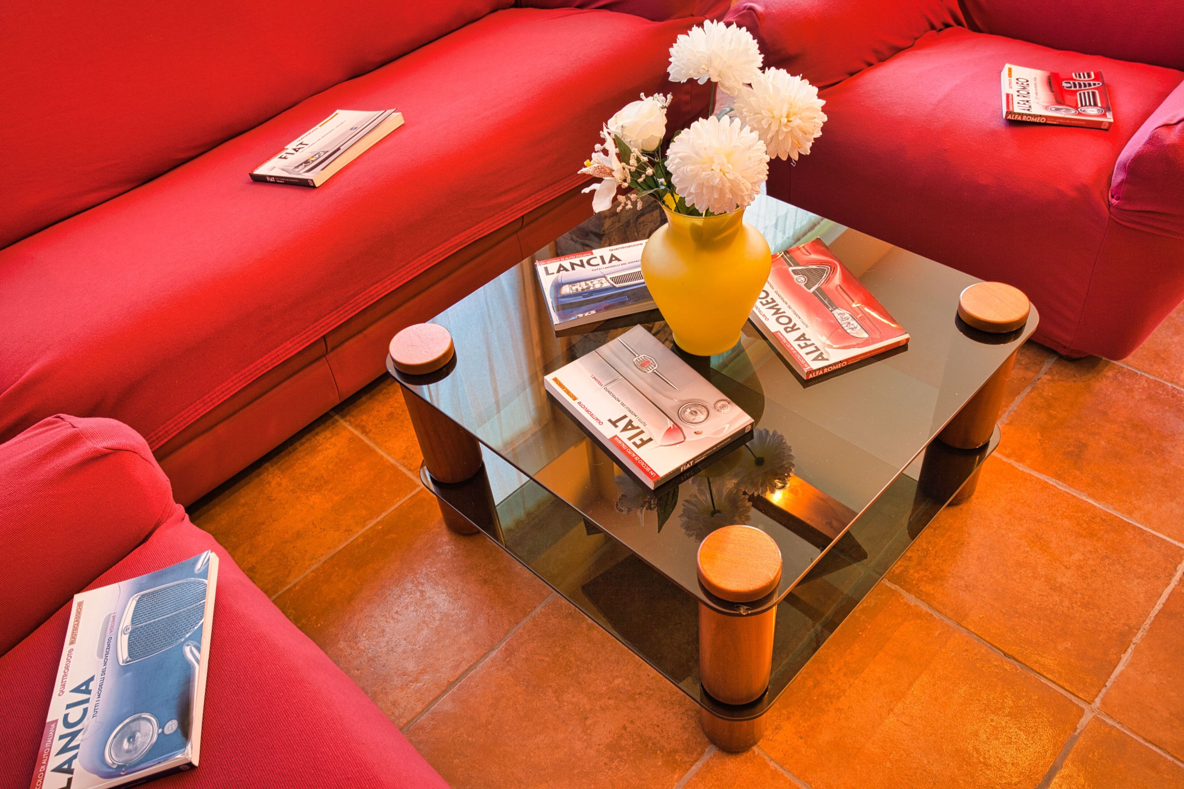 Ein rotes Sofa, ein Glastisch mit einer gelben Vase und Zeitschriften.