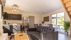 A modern kitchen with dark cabinets, a stainless steel refrigerator, and a dining area with a table set for four. - Chambres Le Tirel (Reux)