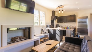 A modern kitchen with a built-in stove, a dining area with a wooden table, and a living room with a sofa. - Chambres Le Tirel (Reux)