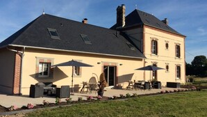 A two-story house with a patio area featuring outdoor furniture and umbrellas. - Chambres Le Tirel (Reux)