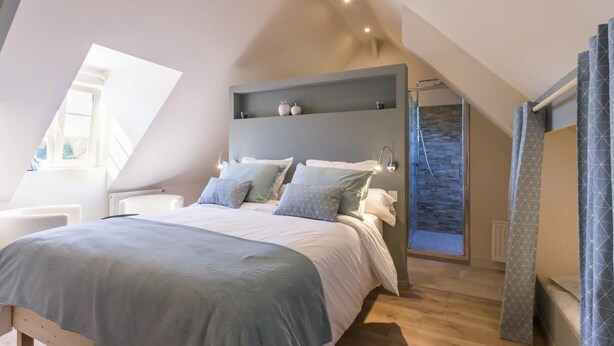 A modern bedroom with a sloped ceiling, a built-in bench, a shower with a stone wall, and a skylight. - Chambres Le Tirel (Reux)