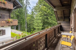 A wooden balcony with a view of a forest, a table with chairs, and a building with a balcony. - Hapimag Resort Sonnleitn (Hermagor-Pressegger See)