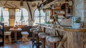 Un rústico espacio de bar con taburetes de madera, una barra y estantes con botellas y vasos.