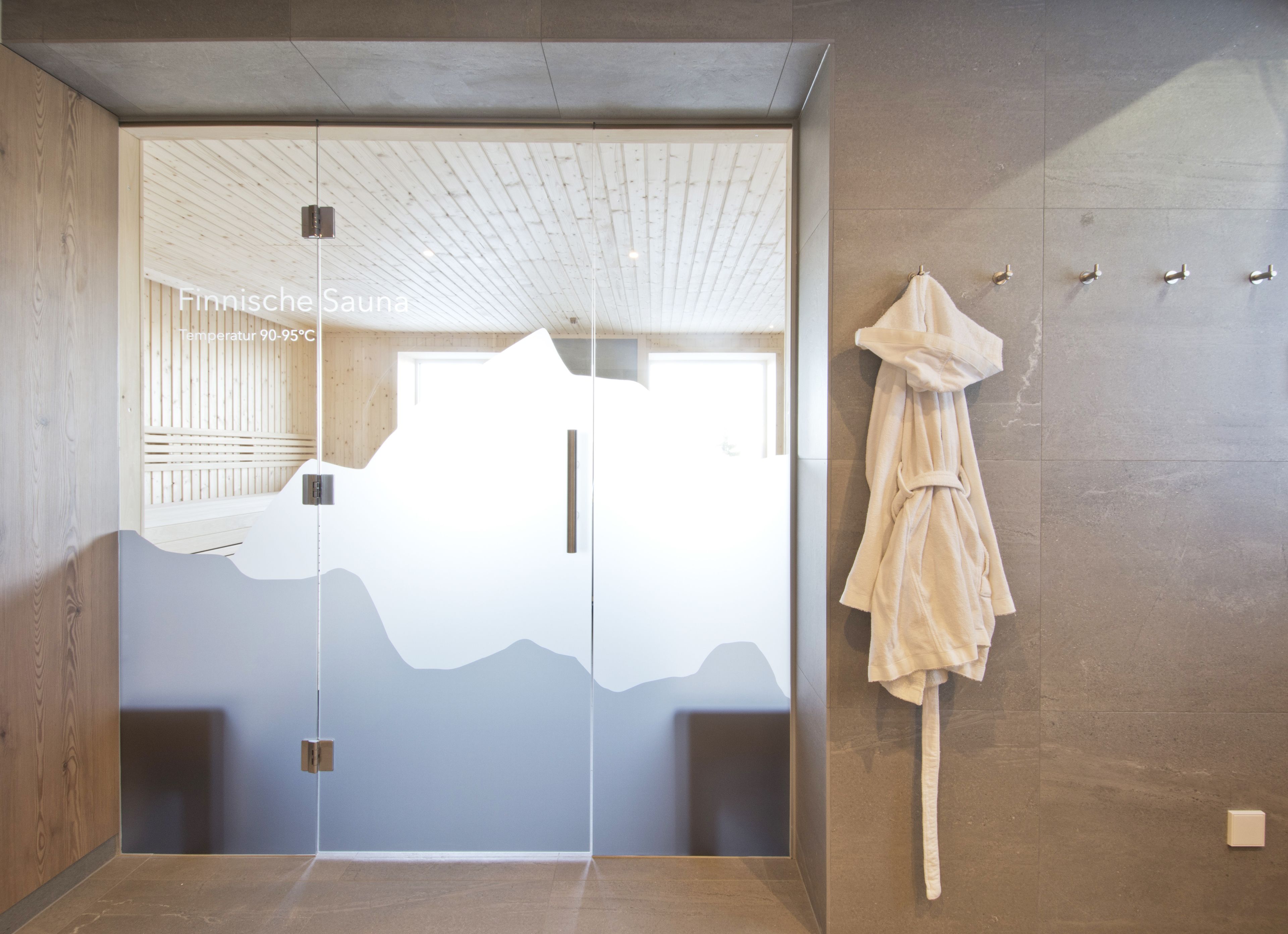 Una sauna con soffitto in legno, una porta in vetro e un porta asciugamani con un asciugamano.