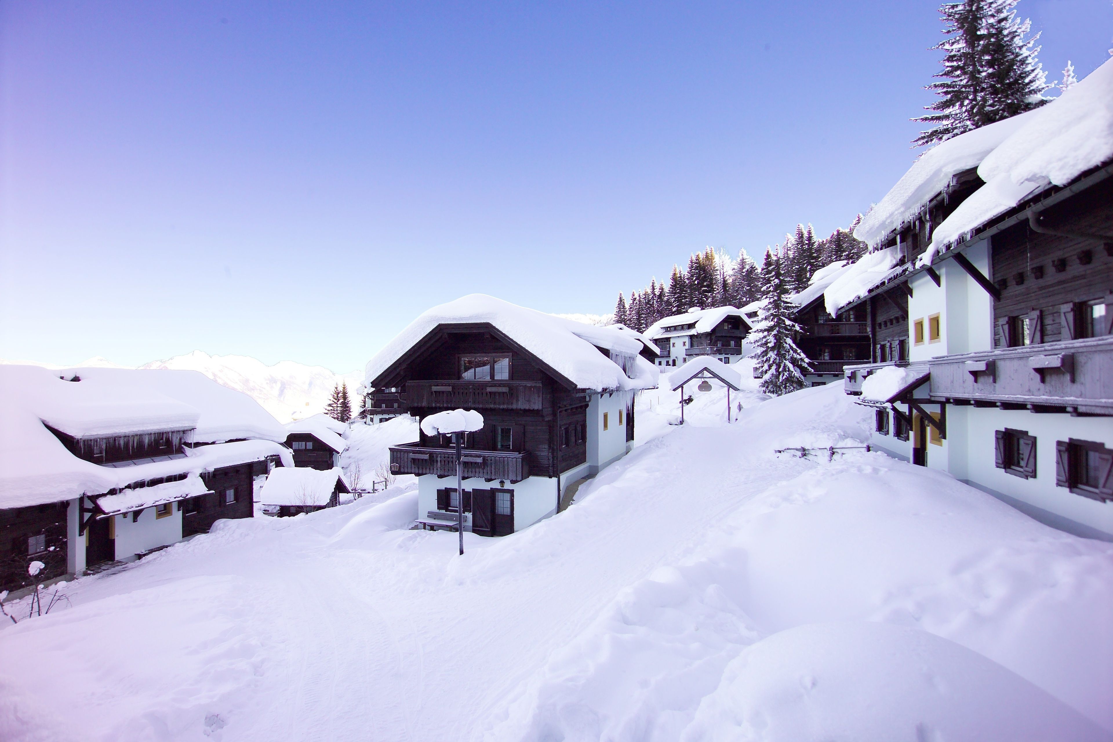 Ein schneebedecktes Dorf mit traditionellen Holzhäusern, blauem Himmel und einer gebirgigen Kulisse.