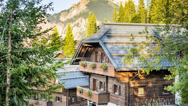 Una cabaña de madera con varios balcones, rodeada de árboles y montañas.