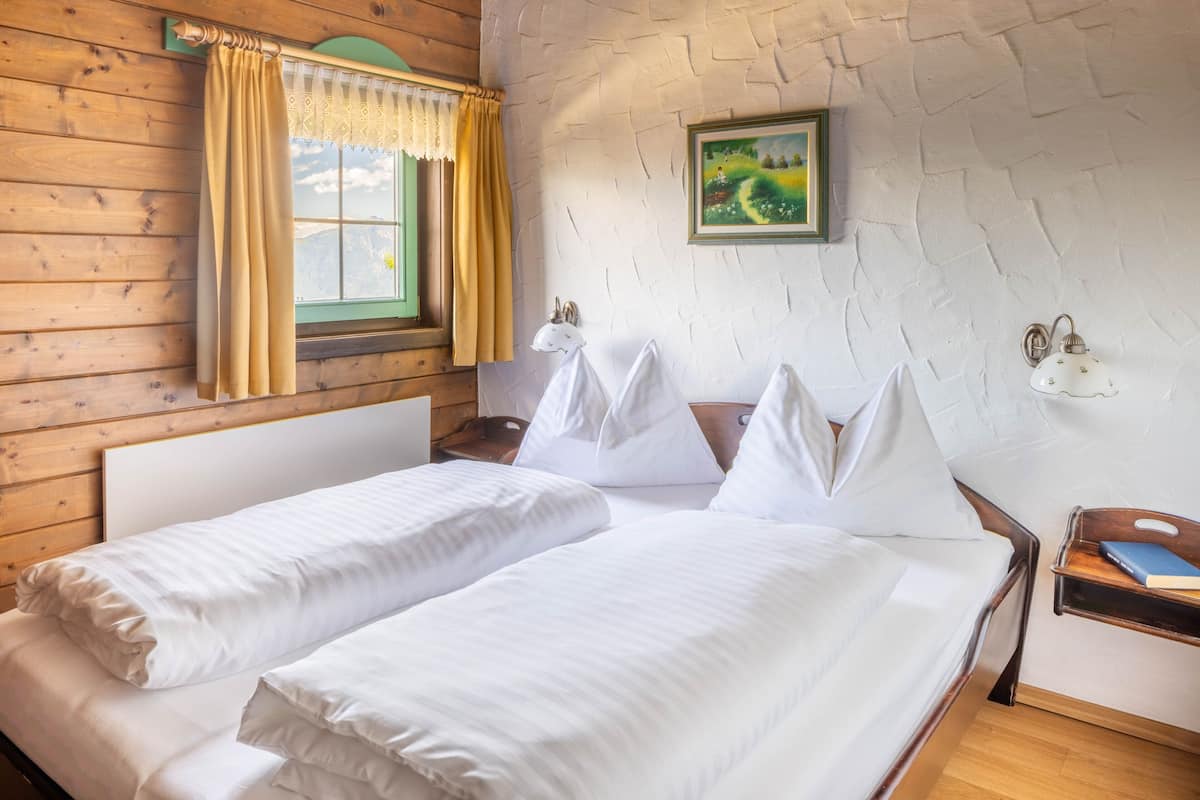 Una habitación con dos camas, paredes de madera, una ventana con cortinas, un cuadro y lámparas fijadas a la pared.