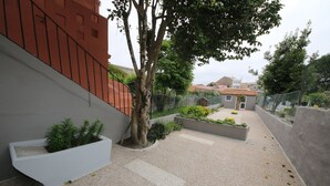 Um pátio com um cachepot branco, uma árvore e uma pequena área de jardim.