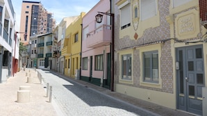 Uma rua de paralelepípedos ladeada por edifícios coloridos, incluindo um edifício com uma placa que diz 'Casa de Santo Antonio'.