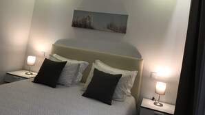 Quarto com cama, duas mesas de cabeceira com abajures, painel de cabeceira e uma obra de arte pendurada na parede.