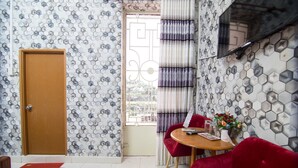 A room with a wooden door, a window with curtains, a round table with a vase of flowers, and red chairs. - RedDoorz near Tan Son Nhat Airport 3 (Ho Chi Minh City)