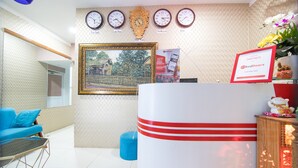 A reception area with a desk, a framed picture, clocks, and a blue sofa. - RedDoorz near Tan Son Nhat Airport 3 (Ho Chi Minh City)