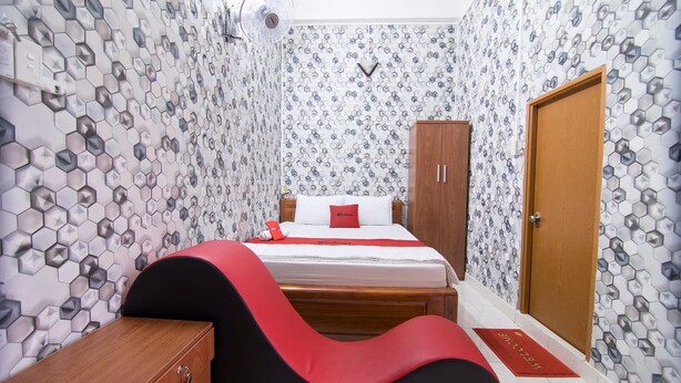 A bedroom with a bed, a wooden wardrobe, a bedside table, and a red and black chair. - RedDoorz near Tan Son Nhat Airport 3 (Ho Chi Minh City)