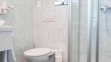 Un baño con inodoro, cabina de ducha de vidrio y piso de baldosas.