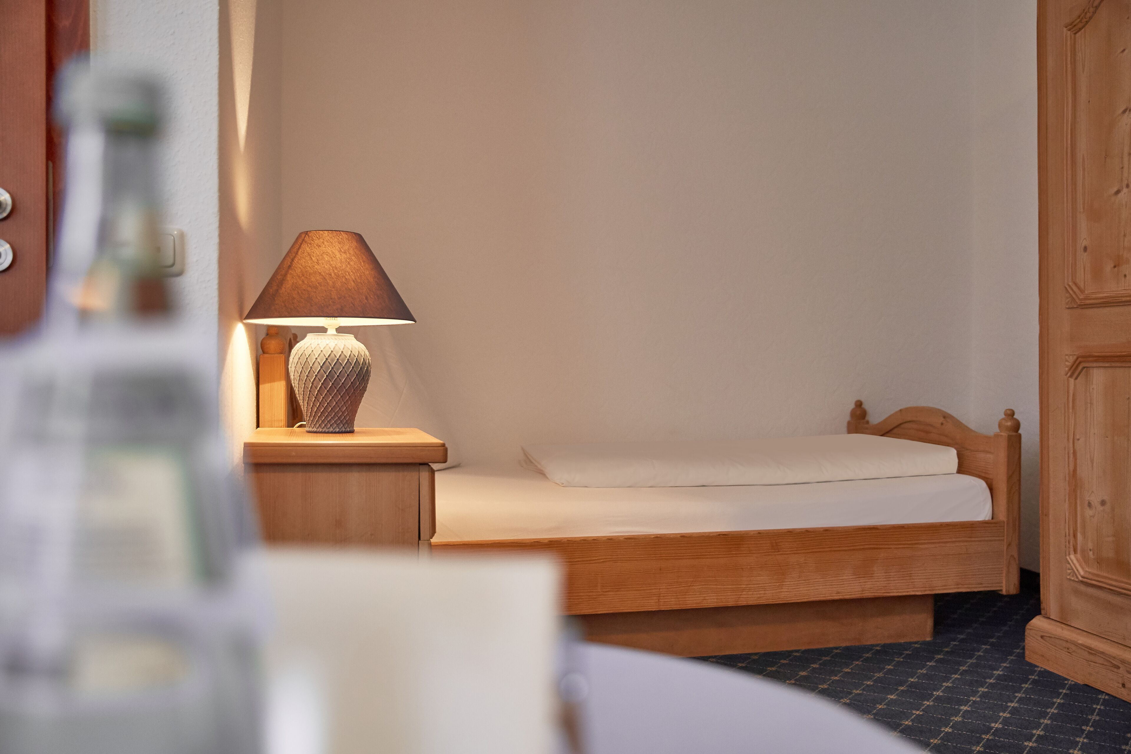 A single bed with a wooden headboard, a bedside table with a lamp, and a wooden wardrobe.
