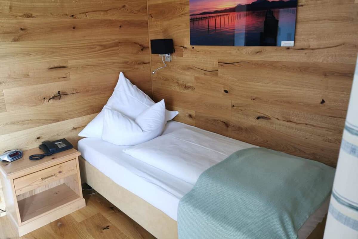 A wooden room with a bed, a nightstand, a lamp, and a painting of a sunset.