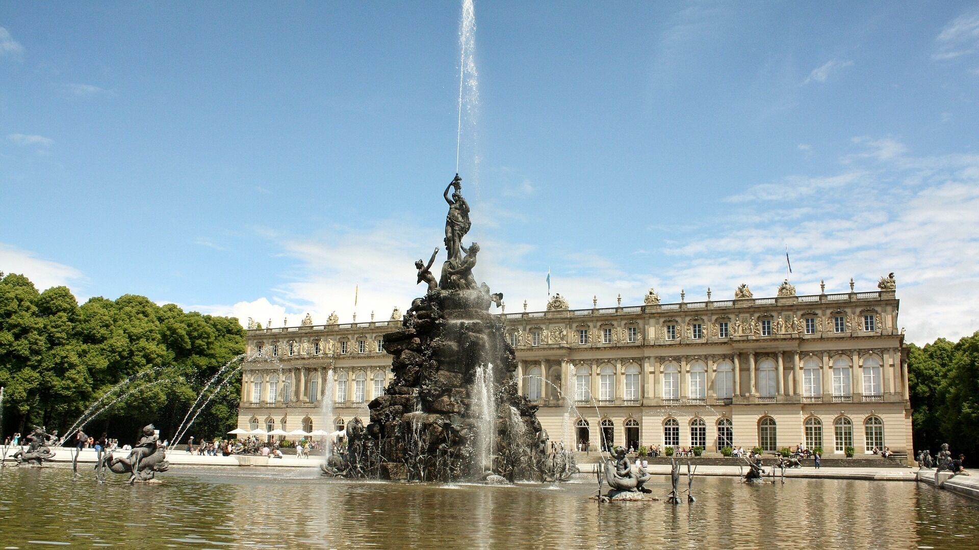 Una gran fuente con múltiples chorros de agua frente a un edificio histórico de arquitectura clásica.