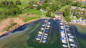 An aerial view of a marina with numerous boats docked, surrounded by green fields and residential buildings. - Zum Fischer am See (Prien am Chiemsee)