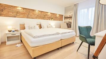 Una habitación de hotel moderna con cabecera de madera, una cama grande con ropa blanca, un sillón verde y vistas a un puente por la ventana.