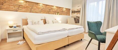 Una habitación de hotel moderna con cabecera de madera, una cama grande con ropa blanca, un sillón verde y vistas a un puente por la ventana.
