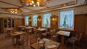 A restaurant with wooden tables and chairs, large windows with curtains, and a traditional ceiling design. - Zum Fischer am See (Prien am Chiemsee)