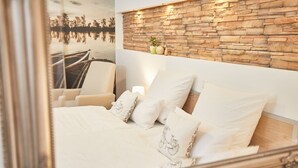 A bedroom with a stone wall, a bed with white linens, and a chair. - Zum Fischer am See (Prien am Chiemsee)