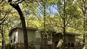 A rustic cabin with a stone foundation, surrounded by a well-maintained lawn and trees. - Peaceful Country Cozy home semi secluded minutes to North end of Lake Ouachita. (Jessieville)