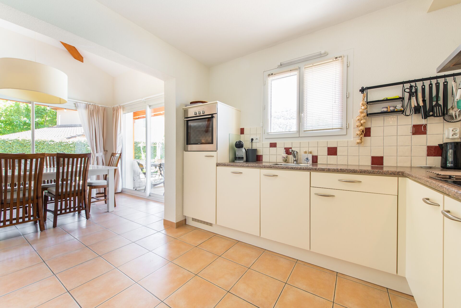 A kitchen with white cabinets, a built-in oven, a coffee maker, and a window with blinds.
