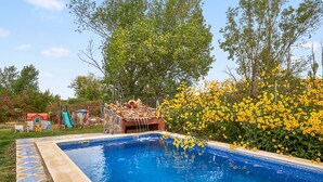 A swimming pool with a stone border, surrounded by greenery and yellow flowers.
