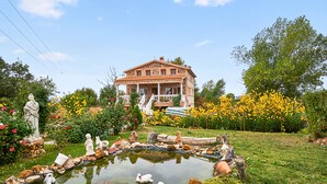 A large house with a garden featuring a pond, statues, and yellow flowers.