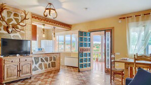 A spacious living room with a television, wooden cabinets, a stone wall, and a view through a glass door.