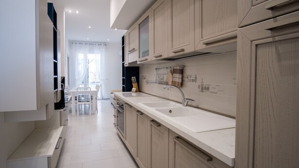 Una cocina moderna con armarios de madera clara, encimeras blancas y horno empotrado.
