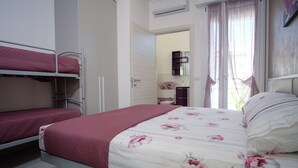 Un dormitorio con literas, una cama grande con ropa de cama floral, un armario y un baño visible a través de una puerta abierta.