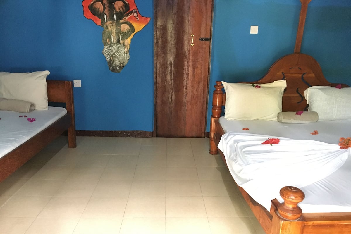 Quarto com duas camas de madeira, parede azul e porta de madeira.