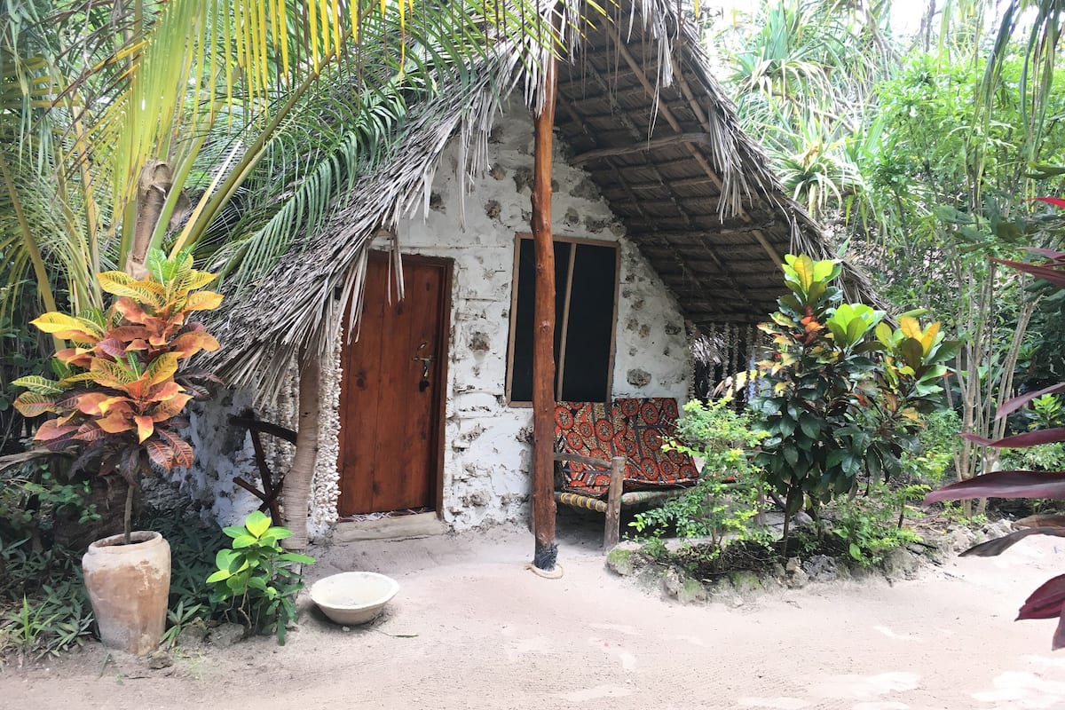 Uma cabana rústica com telhado de palha, porta de madeira e uma pequena janela.