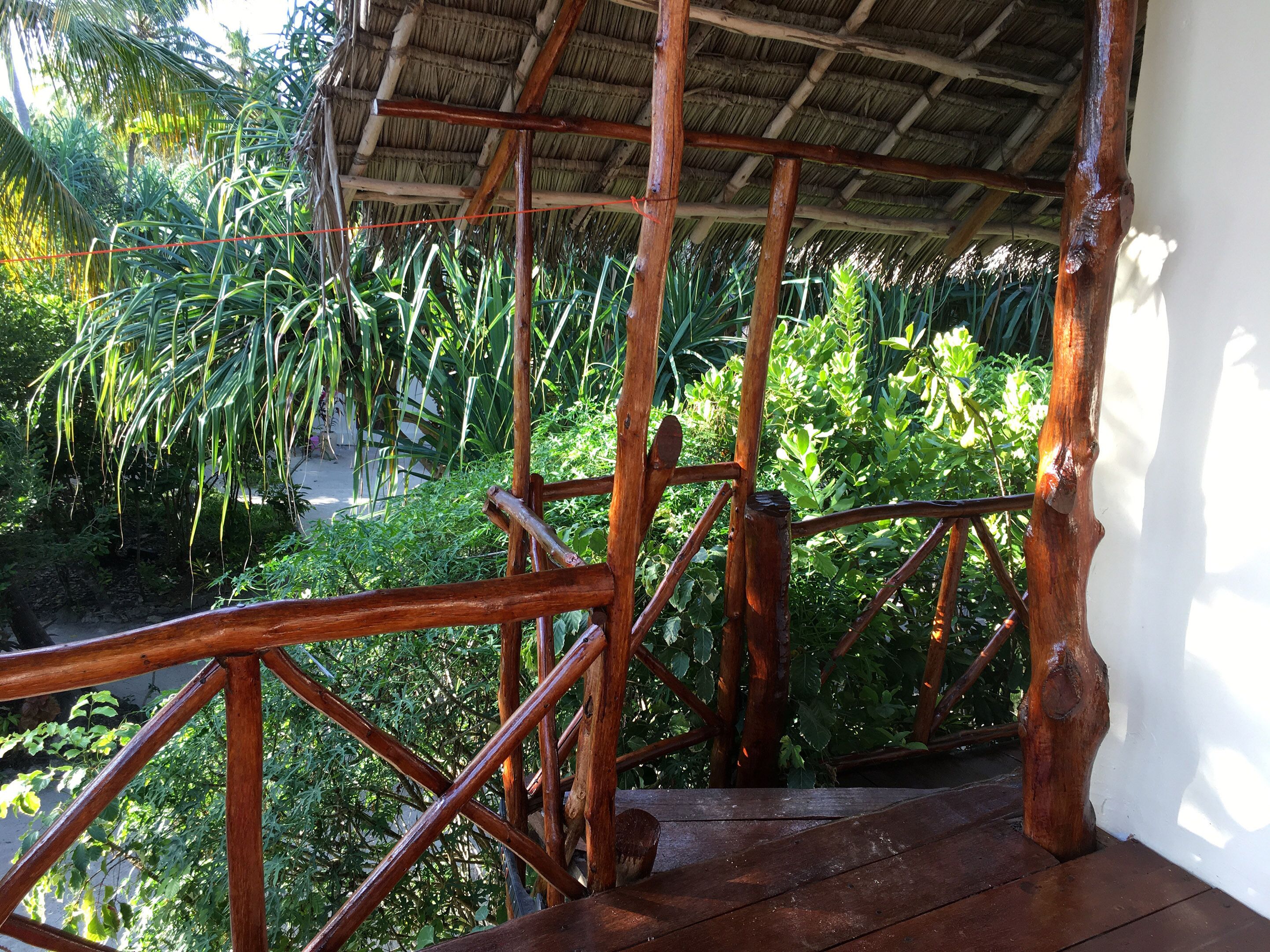 A wooden staircase with a thatched roof, surrounded by lush greenery.