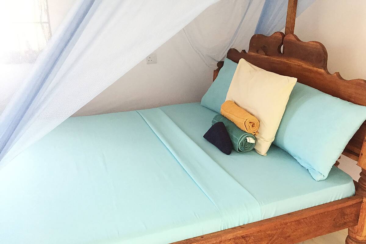 Uma cama com colchão azul claro, cabeceira de madeira e mosquiteiro.
