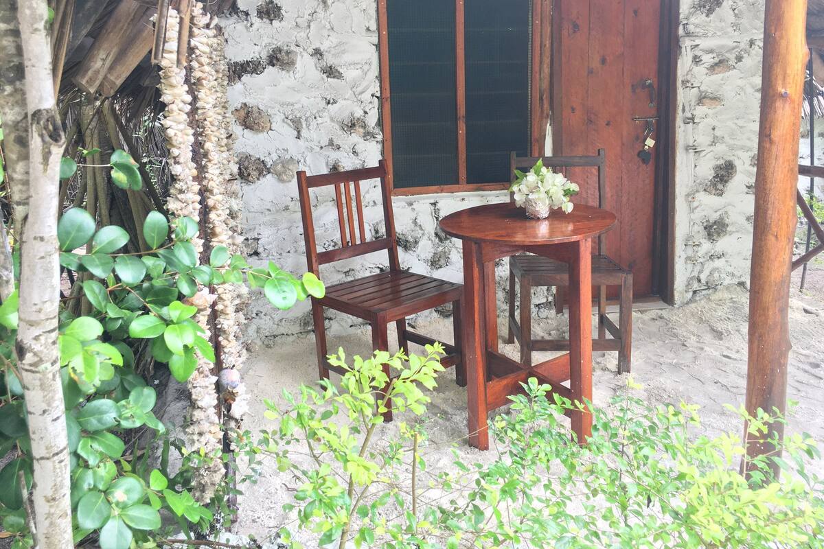 Um conjunto de mesa e cadeiras de madeira montado em frente a um edifício rústico com uma parede de pedra e uma porta de madeira.