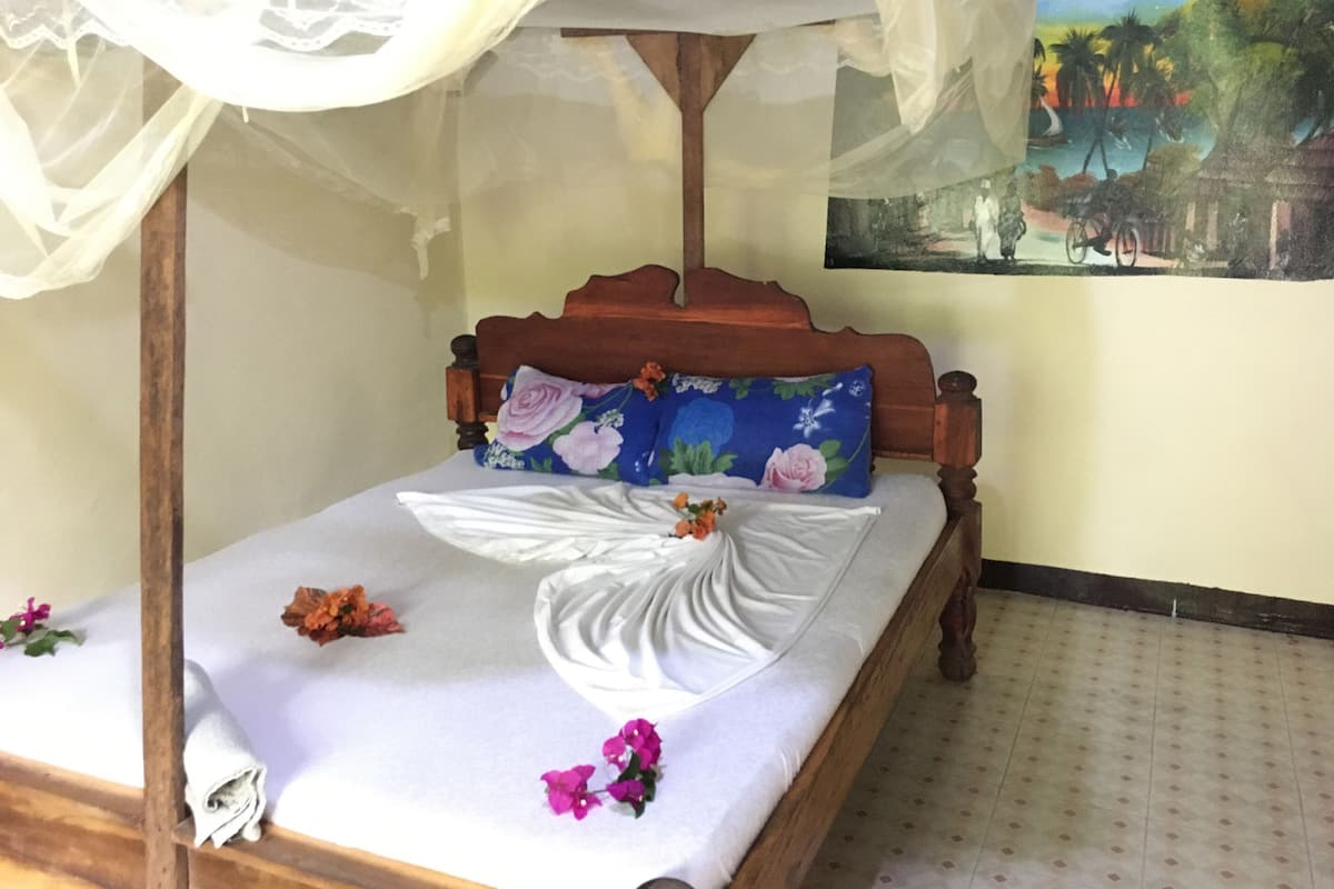 Uma cama com dossel, almofadas florais e um quadro na parede.