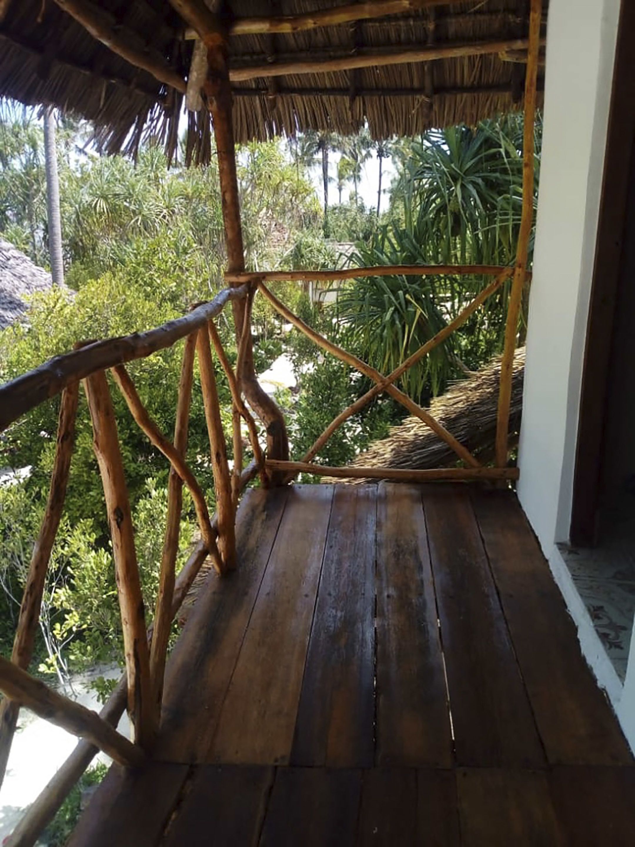 A wooden deck with a thatched roof, surrounded by lush greenery.